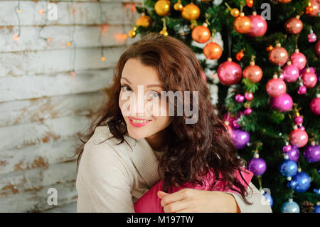 Close-up Portrait of Beautiful Smiling Girl avec les cheveux ondulés sur l'arrière-plan d'un arbre de Noël avec des boules de verre coloré. Banque D'Images