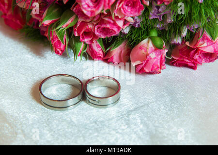 Deux anneaux à l'arrière-plan de fleurs multicolores. Close-up de deux bagues d'Or et mariage bouquet de roses multicolores avec en arrière-plan Banque D'Images