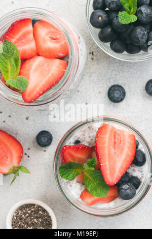 Chia pudding à la fraise avec des bleuets frais et de menthe dans le verre. sur fond de béton lumineux. Vue d'en haut. La saine alimentation, régimes, collation santé, mettre en place Banque D'Images