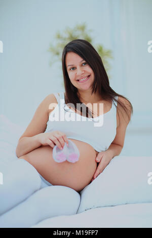 Pregnant woman smiling and holding a baby's futures chaussettes. Banque D'Images