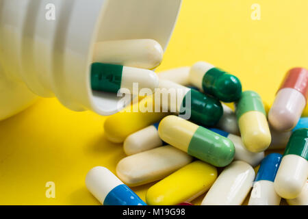 Heap of assorted capsules colorées jaune sur table. Bottle spilling out comprimés. Banque D'Images