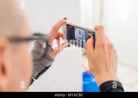 Jeune femme chauve en prenant des photos avec son portable dans les toilettes Banque D'Images