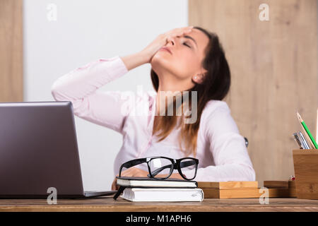 Épuisé Businesswoman With Eyeglasses sur Journal d'un bureau en bois bureau en plus Banque D'Images