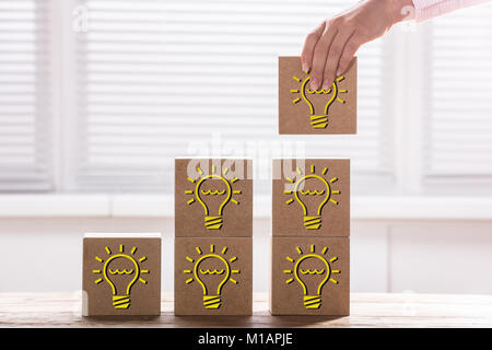 Woman's Hand Holding A Bloc avec ampoule électrique pour compléter le graphique à barres de croissance sur 24 Banque D'Images