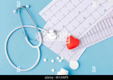 Stéthoscope, papier avec électrocardiogramme, comprimés dispersés et cœur rouge isolé sur fond bleu Banque D'Images