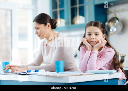 Enfant s'ennuie, debout près de sa maman travaillant Banque D'Images