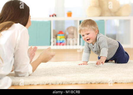 Happy Baby ramper vers sa mère sur un tapis à la maison Banque D'Images