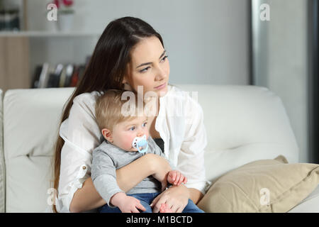 Sad woman avec son bébé assis sur un canapé dans la salle de séjour à la maison Banque D'Images