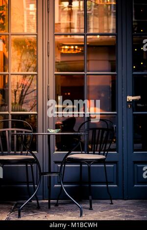 Petite table et chaise en fer forgé dans une rue à l'extérieur de la fenêtre d'une cafétéria et d'une porte en verre avec des reflets rougeoyants de l'hiver des arbres dans une close up v Banque D'Images