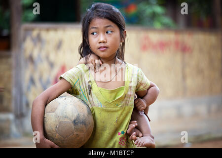 Jeune fille avec un football son littlesister sur le dos dans le Nord du Laos, Lao Village, en Asie du sud-est Banque D'Images