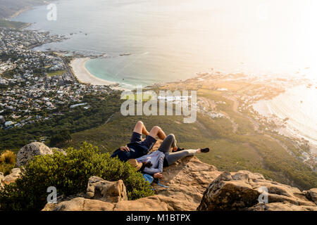 Un couple est reposant sur le haut de la Montagne Lion's Head à Cape Town et d'apprécier le magnifique coucher de soleil avec une vue de Camps Bay et Clifton Beach Banque D'Images