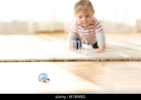 Bébé curieux ramper vers une sucette sale sur le plancher à la maison Banque D'Images