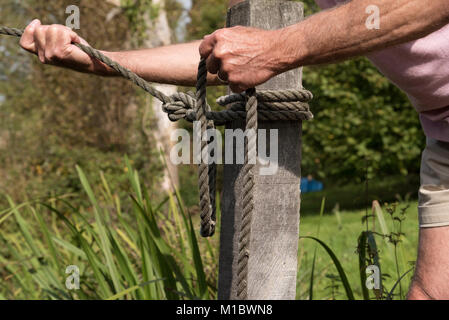 Ligne de mouillage qui se tient entre les mains de l'homme est attaché à un poteau avec un tour mort et deux demi-clefs knot Banque D'Images