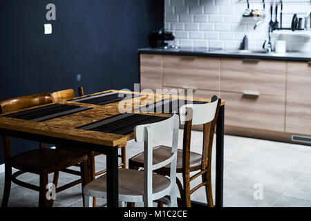 La cuisine est dans un style loft avec des murs de brique et de béton et de tuiles. Il y a une table de cuisine noir blanc avec des chaises. Banque D'Images