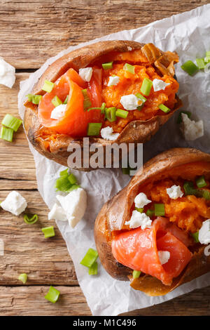 Les aliments biologiques : baked sweet potato farcies de poisson rouge et oignon vert close-up sur le papier sur la table. Haut Vertical Vue de dessus Banque D'Images