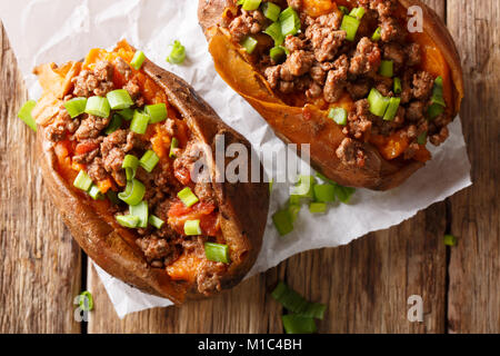 Aliments biologiques : au four farcies de patate douce avec du boeuf haché et l'oignon vert close-up sur le papier sur la table. haut horizontale Vue de dessus Banque D'Images