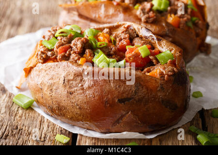 Les patates douces cuites au four farcies au boeuf haché avec les tomates et oignons macro sur papier sur une table horizontale. Banque D'Images