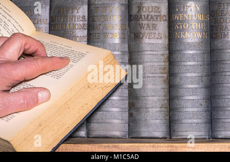 La main de l'homme sur un livre ouvert, publié en anglais, avec une étagère de livres vintage dos dur dans l'arrière-plan. Angleterre, Royaume-Uni. Banque D'Images