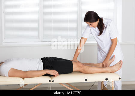 Jeune femme Physiothérapeute Massaging Man's Leg In Clinic Banque D'Images