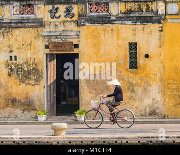 Une dame vietnamienne qui fait du vélo la vie quotidienne devant un vieux bâtiment dans la vieille ville de hoi an .vietnam Banque D'Images