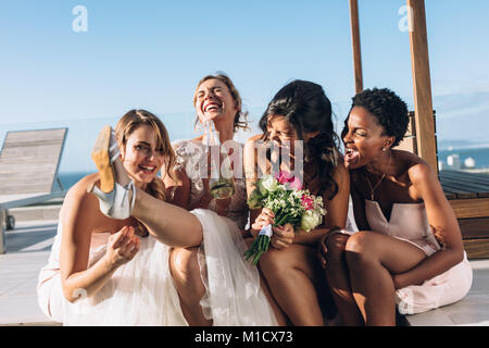 Mariée boire du vin alors qu'il était assis sur le toit avec des demoiselles. Mariée et demoiselles d'amusement avant mariage. Banque D'Images