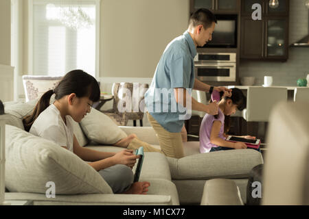 Girl using digital tablet while père peignant ses cheveux filles Banque D'Images