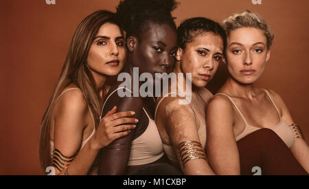 Portrait de jeunes femmes avec différents types de peau sur fond brun. Groupe diversifié de females looking at camera. Banque D'Images