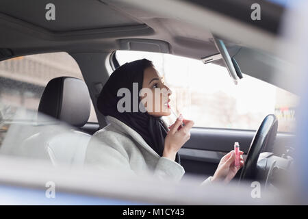 Femme en hijab applying lipstick Banque D'Images