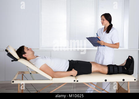 Jeune femme orthopédiste debout près de Male Patient With Clipboard Banque D'Images