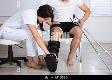 Jeune femme médecin mettre à pied orthèse sur la jambe de la personne à l'hôpital Banque D'Images