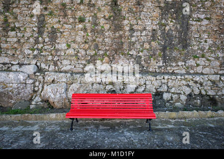 Banc peint rouge contre un vieux mur de pierre. Banque D'Images