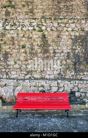 Banc peint rouge contre un vieux mur de pierre. Banque D'Images