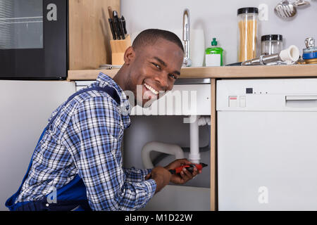 African Male fixation tuyau plombier lavabo dans la cuisine Banque D'Images