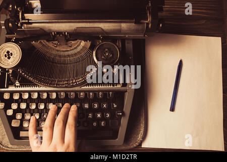 Main sur une machine à écrire sur un fond de bois et une feuille blanche et stylo à bille. Style rétro. Banque D'Images