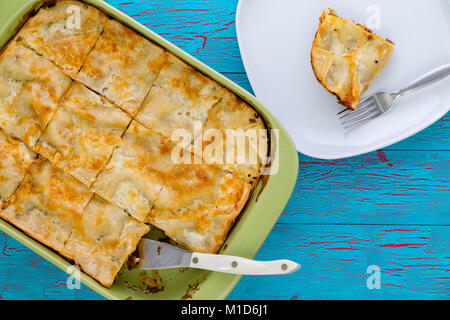 Tarte fraîchement faite avec une pâtisserie haut coupé en portions dans un plat allant au four, prêt à servir avec une seule tranche servi sur une plaque blanche avec fourchette alongs Banque D'Images