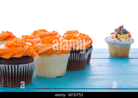 Des cupcakes avec glaçage orange colorées décoratives disposées en alternance de vanille et chocolat sur une table en bois bleu with copy space Banque D'Images