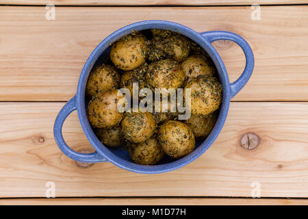 Pot bleu plein de pommes de terre bouillies bébé assaisonné recouvert d'herbes et d'épices diverses vues de dessus sur une table en bois avec les poignées placées diagona Banque D'Images