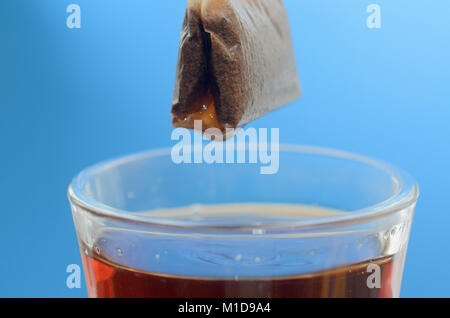 Un sachet de thé sur une tasse en verre avec de l'eau chaude sur un fond bleu. Banque D'Images