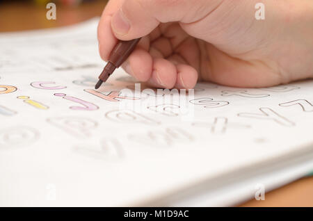 La main d'un enfant écrit et affiche English lettres d'un ordinateur portable et de l'alphabet avec un crayon et un stylo-feutre. Banque D'Images