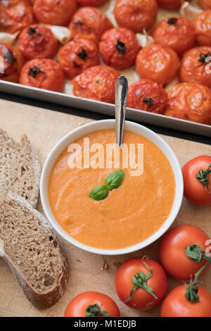 Soupe tomate et basilic fait maison avec du pain de seigle à côté de tomates grillées et l'ail dans une plaque de cuisson sur un fond d'ardoise. Banque D'Images