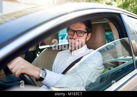 Smiling young man au volant de sa voiture dans les rues de la ville Banque D'Images