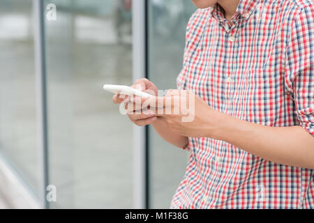 Un homme lit un message texte à l'extérieur du bureau permanent Banque D'Images