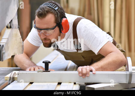 Vêtements de travail dans jeune menuisier travaille dans la menuiserie sur une machine de ponçage - vêtements de travail avec des lunettes de protection et la protection des oreilles Banque D'Images