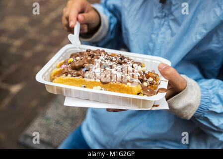 Petite fille manger une gaufre de chocolat sur une rue de la ville médiévale de Bruges, Belgique Banque D'Images