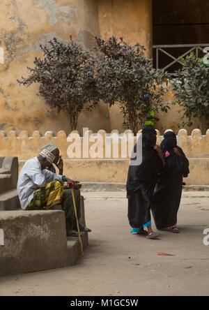 Les femmes musulmanes en burqa en passant en face de gens assis sur un banc dans la rue, comté de Lamu, Kenya, Lamu Town Banque D'Images