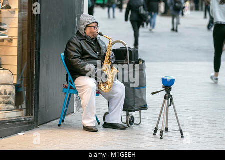 Un musicien ambulant de rue jouant son saxophone espérant aux dons en espèces dans les rues du centre-ville de Liverpool, Royaume-Uni Banque D'Images