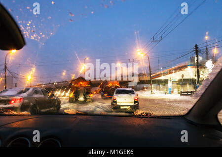 Voir des voitures et machines de nettoyage de rue par le biais de pare-brise humide pendant la conduite automobile sur road dans la ville de Moscou dans la soirée d'hiver dans la neige Banque D'Images