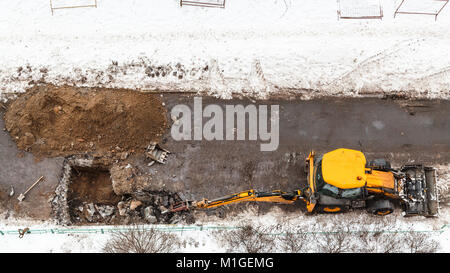 Au-dessus du tracteur routier creuser pour changer les tuyaux d'égout en hiver dans la ville de Moscou Banque D'Images