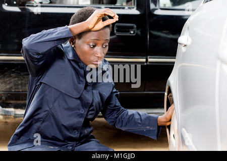 Jeune femme libre de changer le mécanicien pneu d'une voiture dans son garage. Banque D'Images
