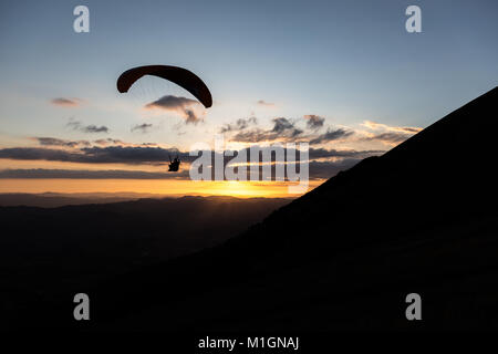 Beau coup d'une silhouette parapente voler au-dessus de Monte Cucco (Ombrie, Italie) avec le coucher du soleil sur l'arrière-plan, avec de belles couleurs et les tons sombres Banque D'Images